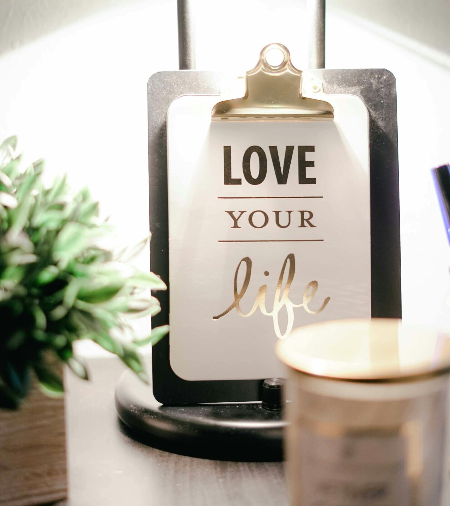 A warmly lit desk setup featuring a lamp, inspirational clipboard, and decor for a cozy ambiance.